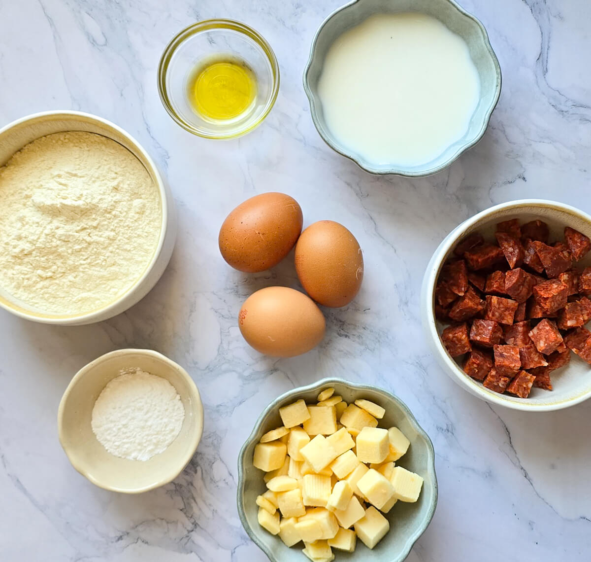Des ingrédients sur une surface blanche marbrée, pour préparer un cake au chorizo.