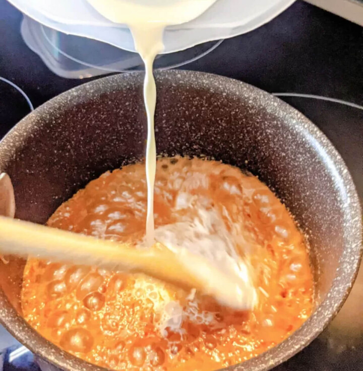 Un filet de crème liquide versé dans une casserole de sucre caramélisé bouillant pour la préparation d'un caramel au beurre salé maison.