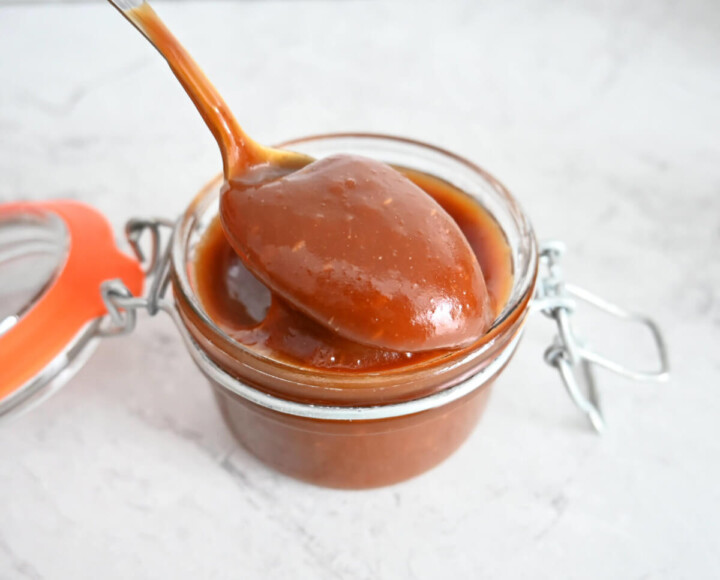 Une cuillère tenant du caramel beurre salé, dans un bocal en verre.