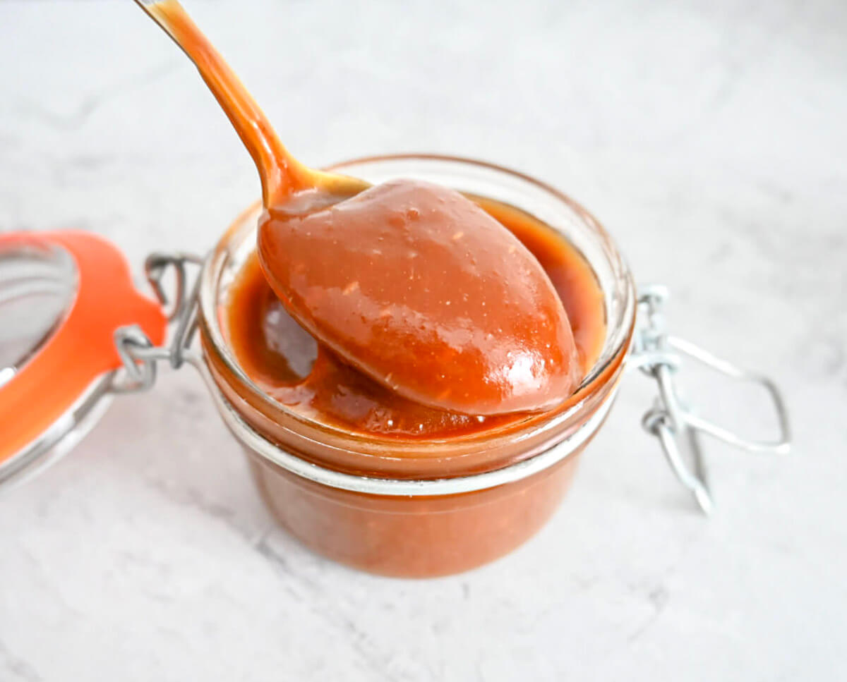 Sauce caramel au beurre salé nappant doucement le bord d'un pot en verre avec une texture lisse et brillante.