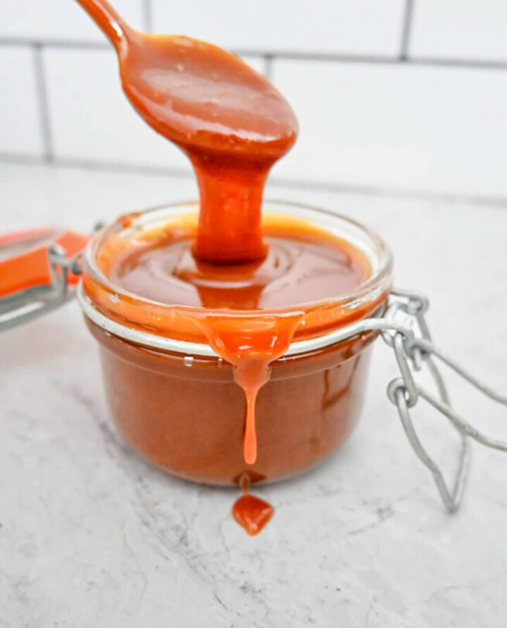 Une cuillère en métal soulève une généreuse dose de sauce caramel au beurre salé onctueuse au-dessus d'un bocal en verre.