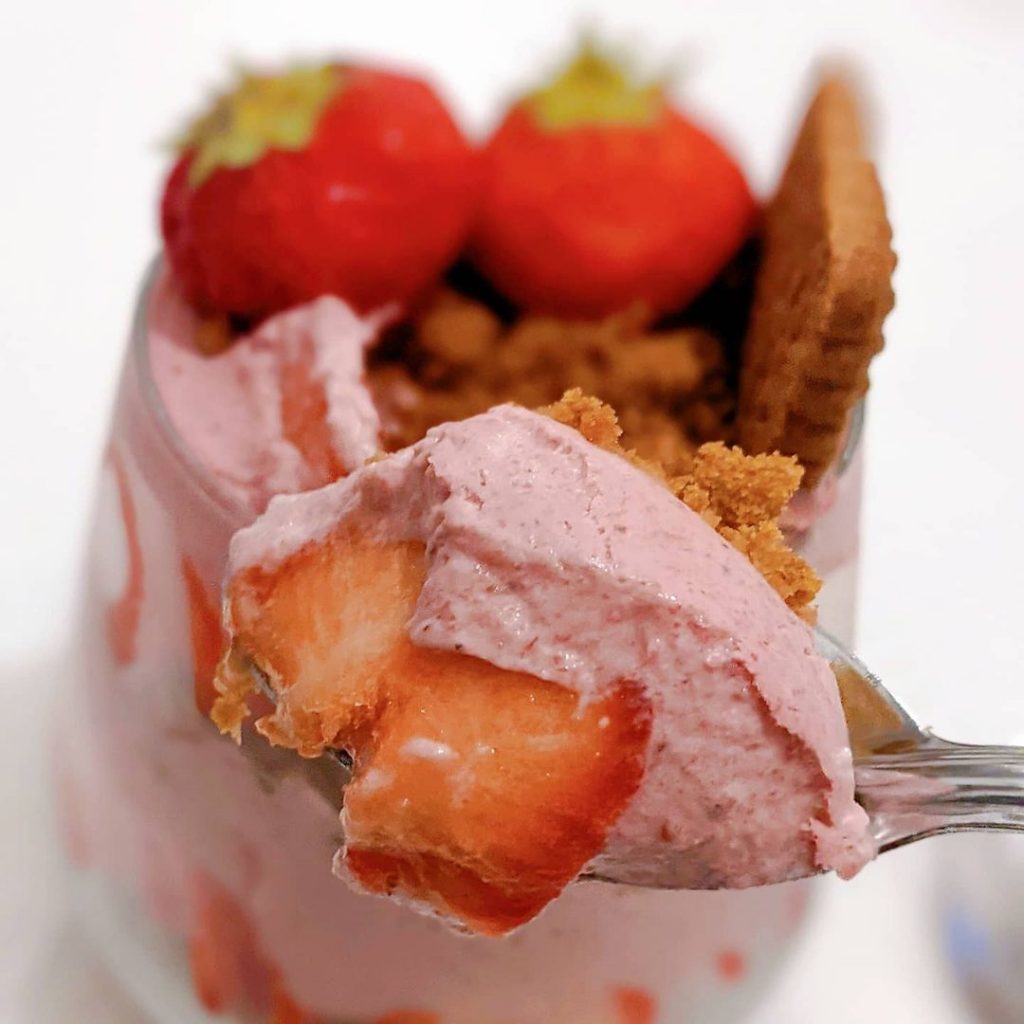 Une cuillère tenant un morceau de verrine fraises Spéculoos maison.
