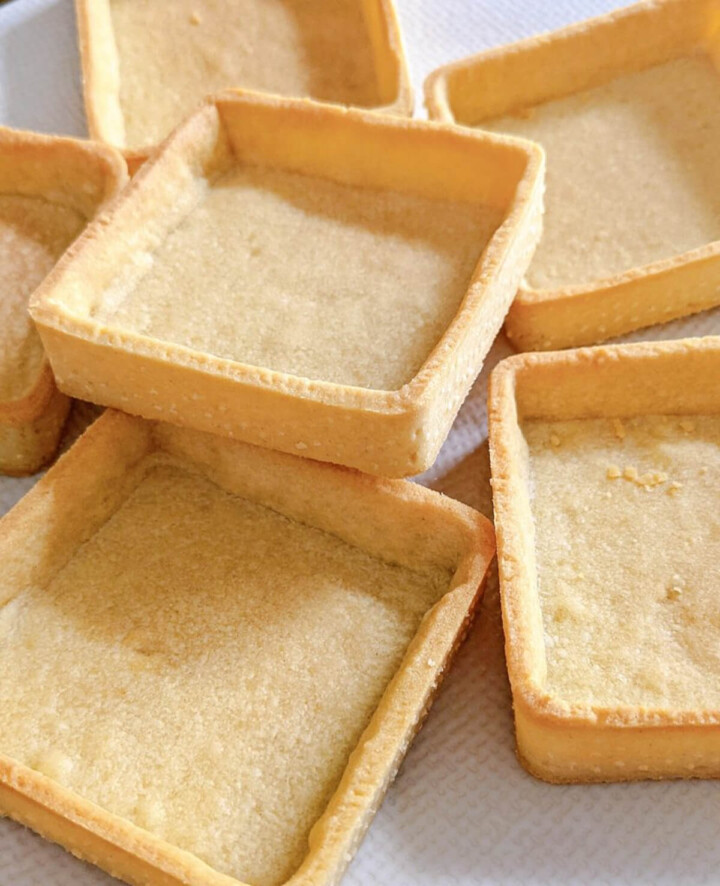 Plusieurs fonds de tartelettes carrés en pâte sucrée maison, cuits à blanc et bien dorés, disposés sur une grille.