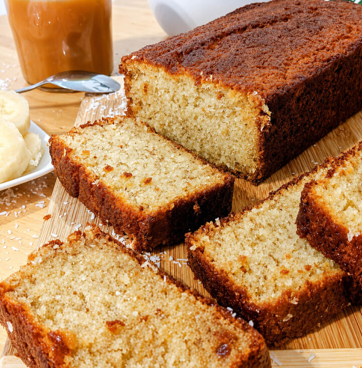 Un cake banane noix de coco très moelleux, coupé en tranches, sur une planche de bois.