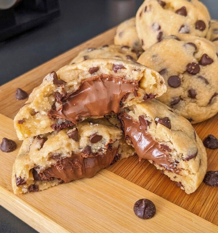 Gros plan de cookies moelleux fourrés au Nutella sur une planche en bois, avec un cœur fondant à la pâte à tartiner.