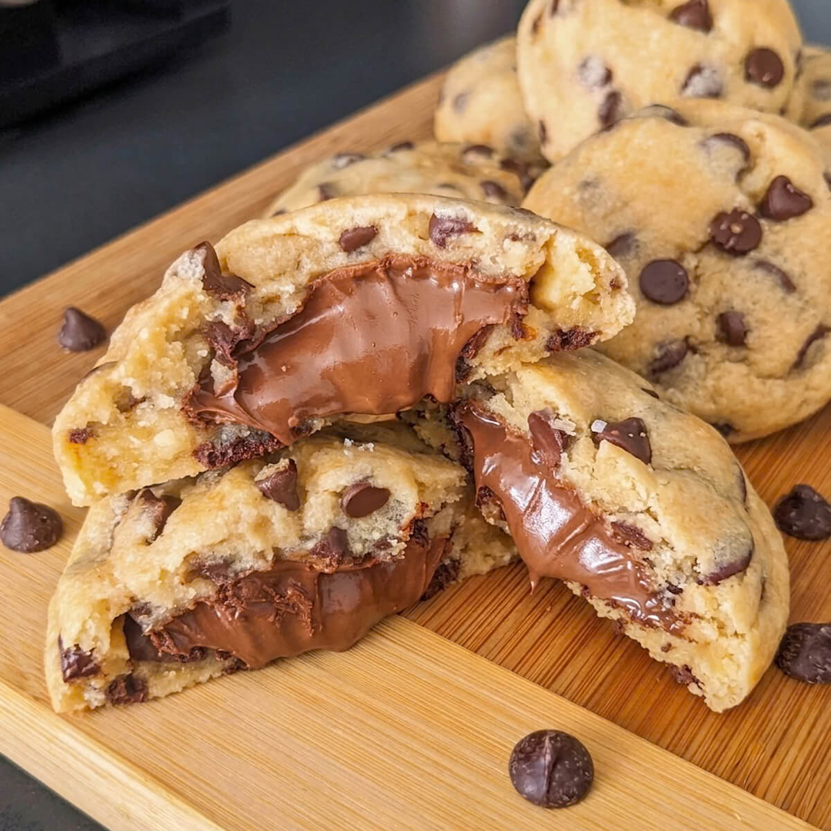 Gros plan de cookies moelleux fourrés au Nutella sur une planche en bois, avec un cœur fondant à la pâte à tartiner.