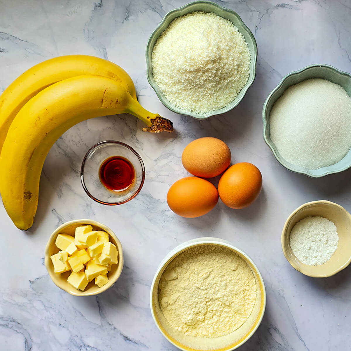 Des ingrédients pour réaliser un gâteau banane noix de coco, sur un fond blanc marbré.