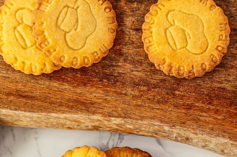 Plusieurs sablés bretons dorés posés sur une planche en bois, dont un biscuit cassé en deux montrant une texture sableuse et croustillante.