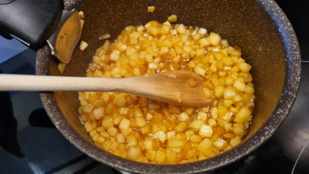Une casserole avec des pommes caraméliser, et une cuillère en bois, pour réaliser des tartelettes facon tarte tatin aux pommes.