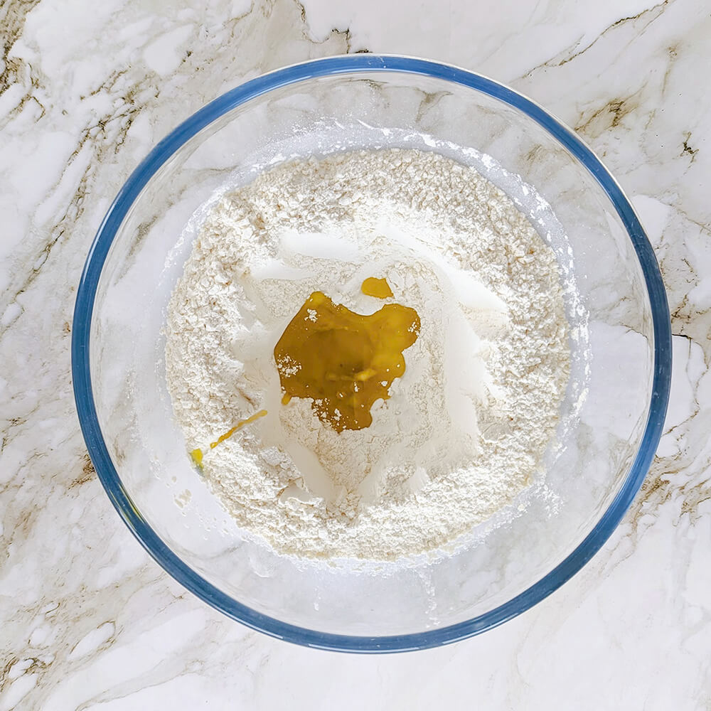 Ingrédients pour petits pains à la poêle avec un puits de farine blanche contenant de l'huile d'olive dorée au centre d'un saladier en verre.