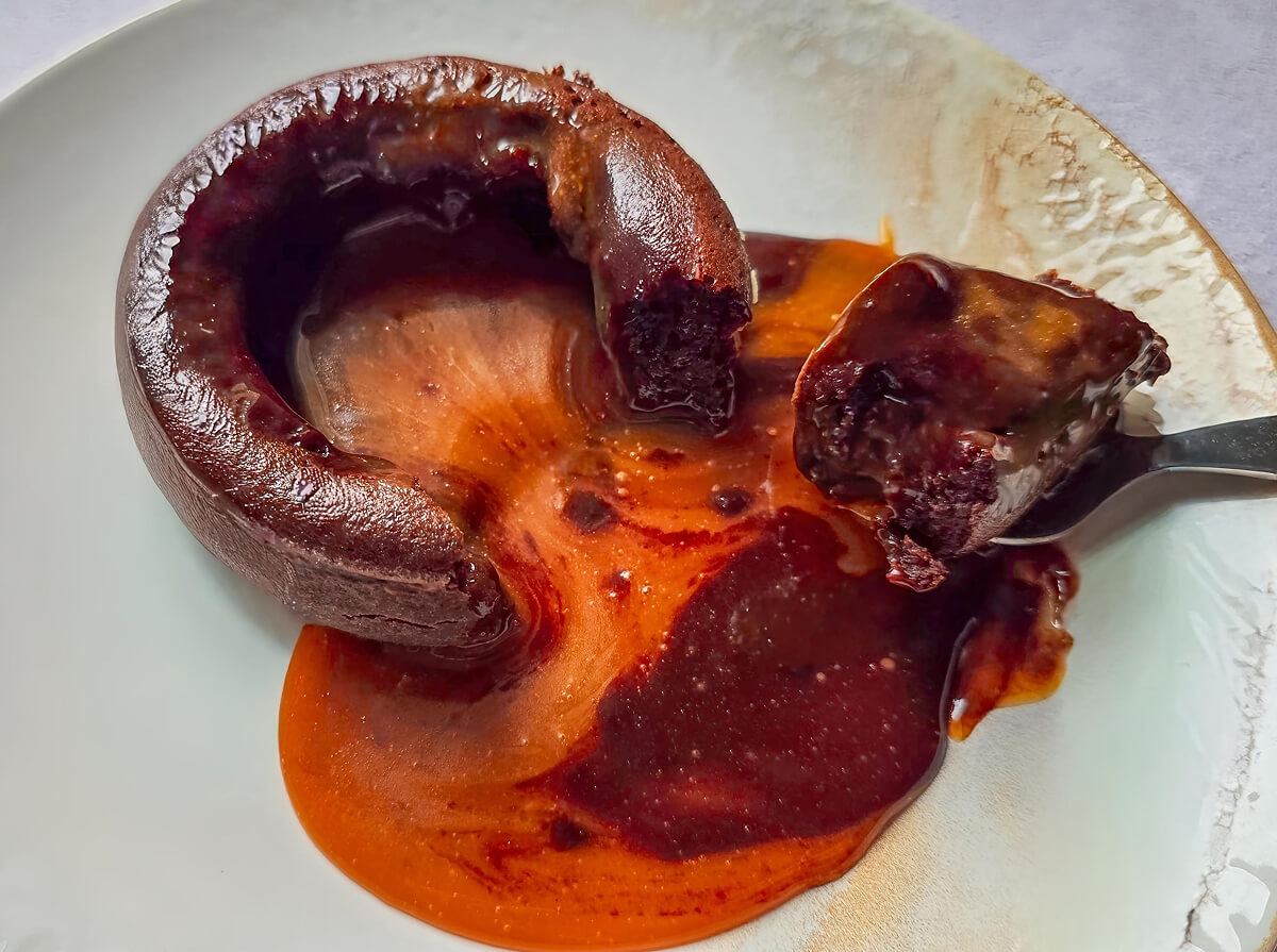 Un fondant chocolat caramel dégoulinant dans une assiette blanche, avec petite cuillère.