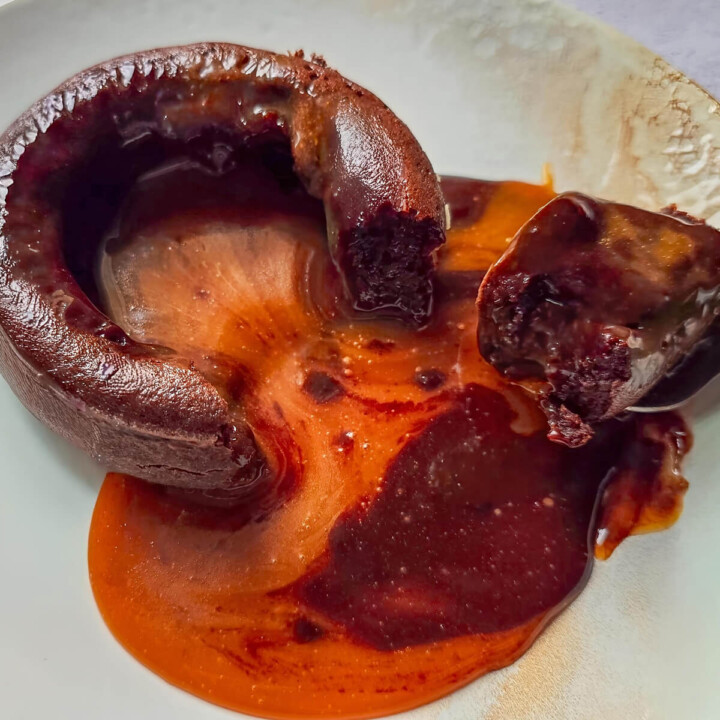 Un fondant chocolat caramel dégoulinant dans une assiette blanche, avec petite cuillère.