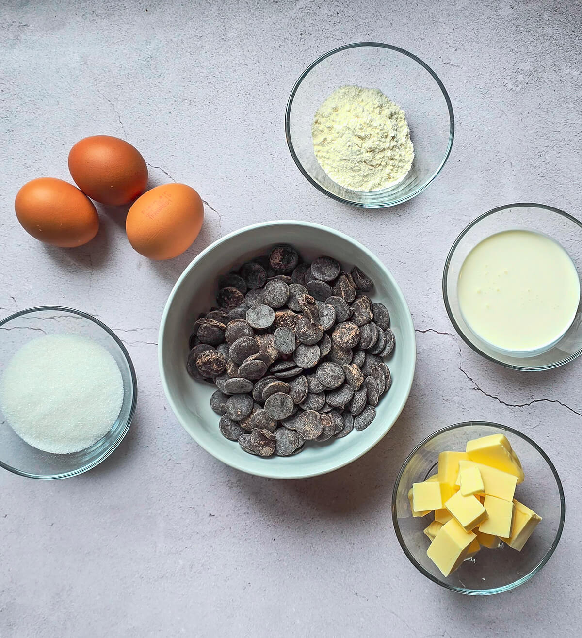 Des ingrédients pour une recette de coulants au chocolat, sur un fond gris clair.