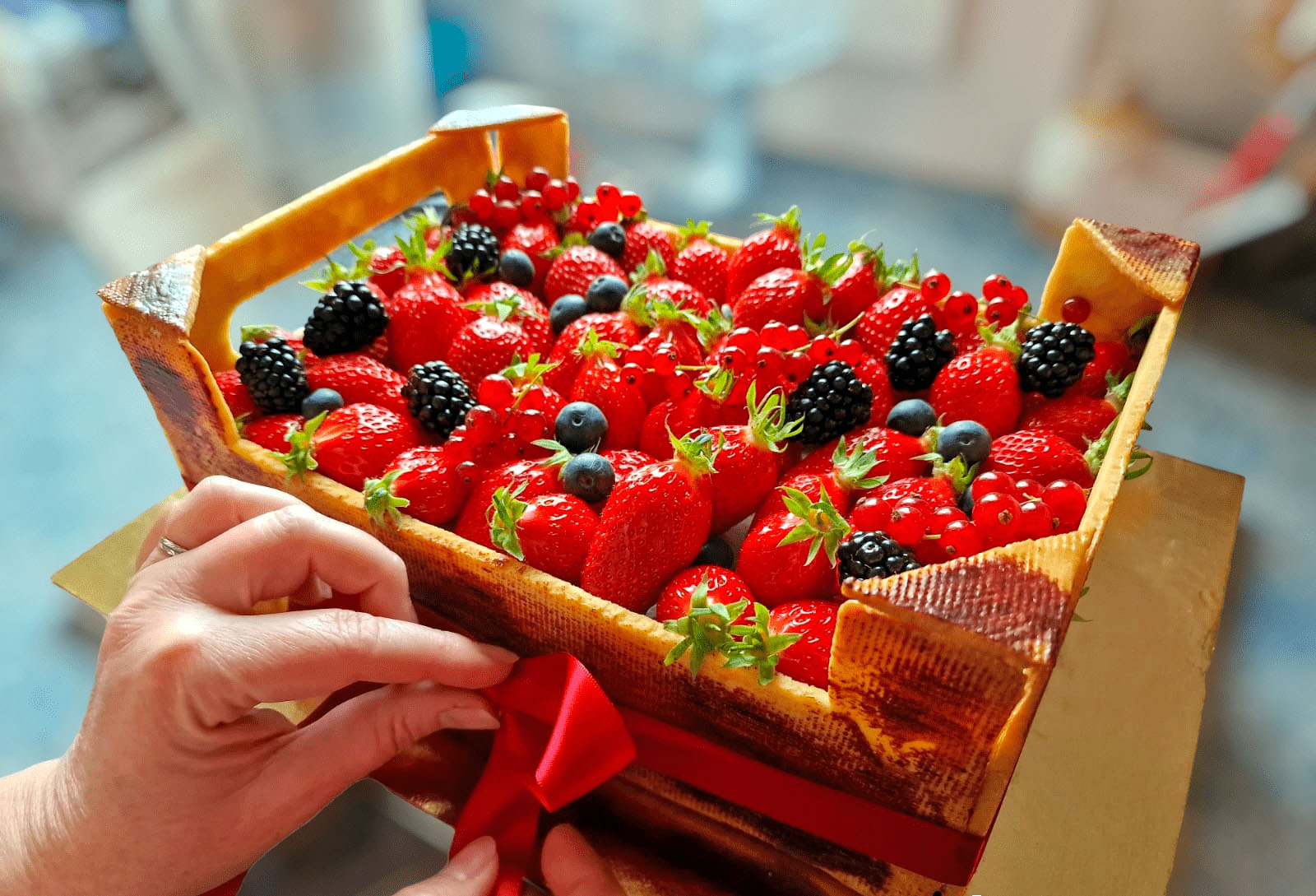 Deux mains faisant un noeu avec un ruban rouge autour d'un fraisier cagette