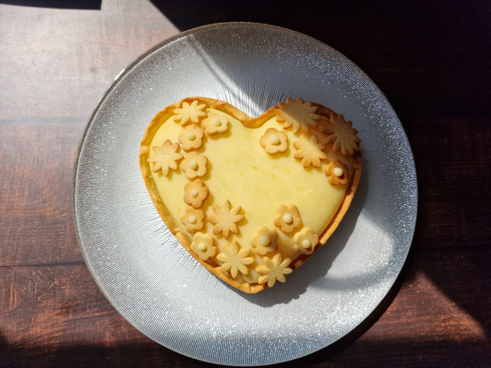 Une tarte au citron en forme de coeur dans une assiette pailletée grise.