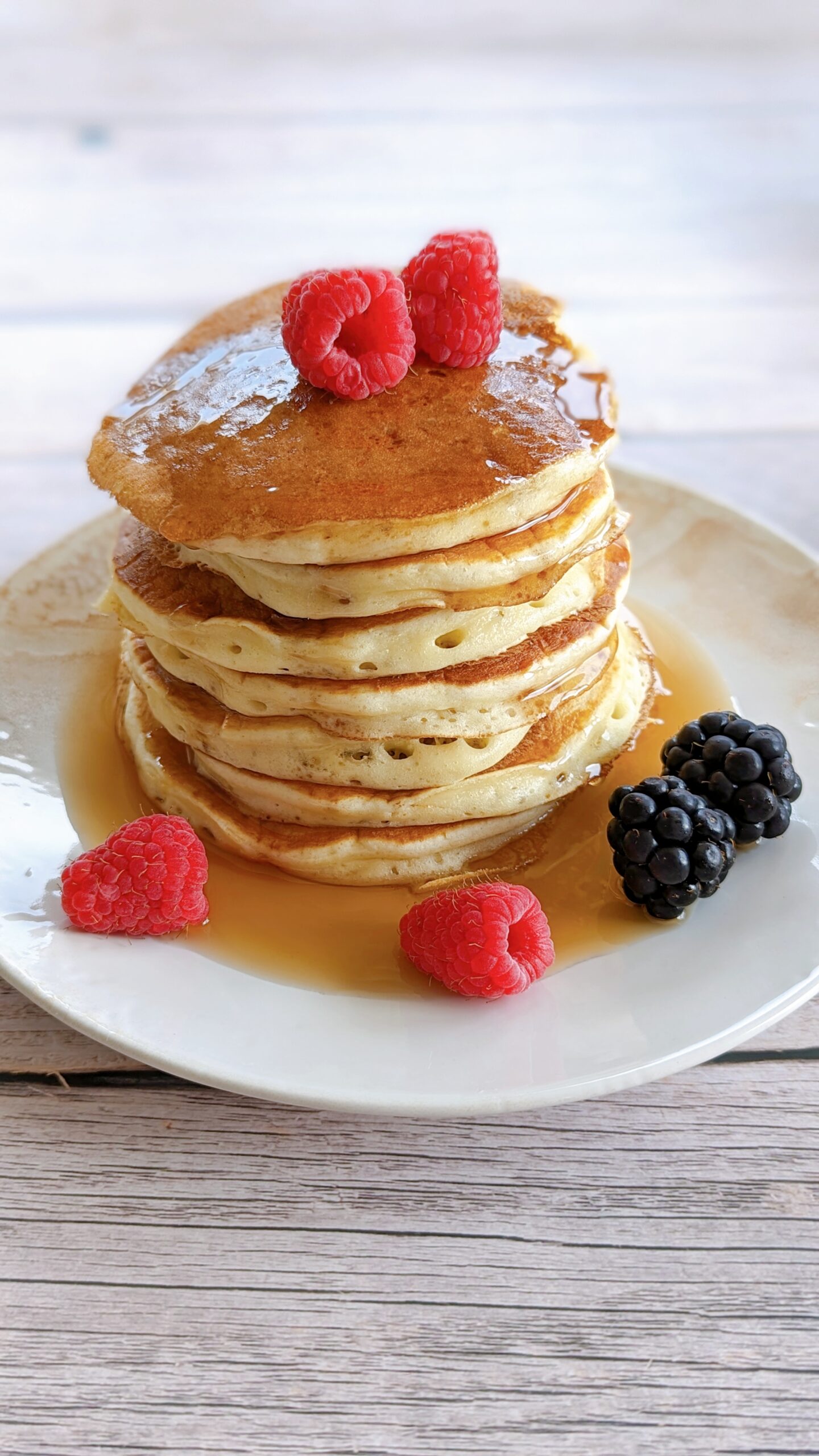 Des pancakes fluffy dans une assiette avec des fruits rouges et du sirop d'érable.