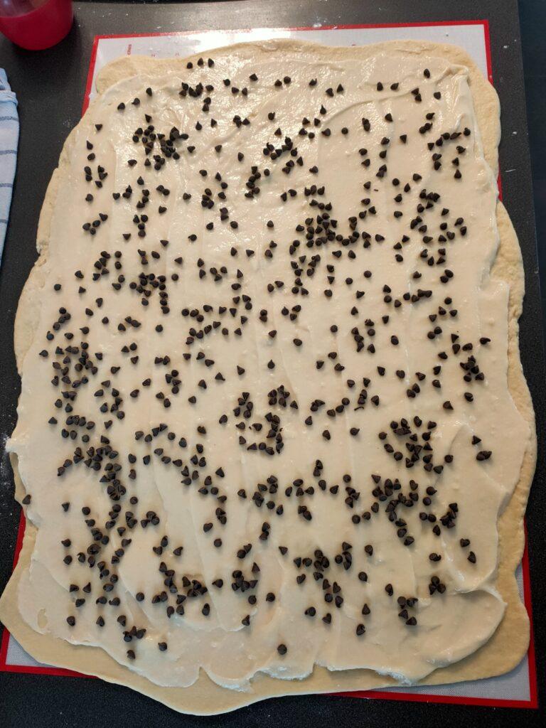 Un gâteau chinois étalé avec de la crème pâtissière et des pépites de chocolat sur un plan de travail.