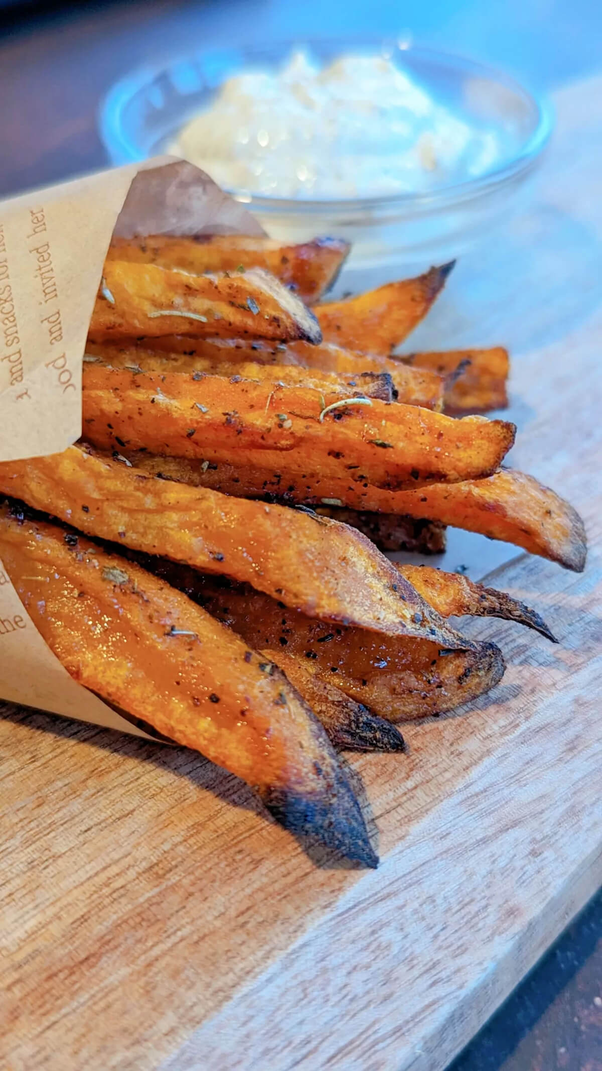Des frites de patates douces dans un papier journal, sur une planche de bois.