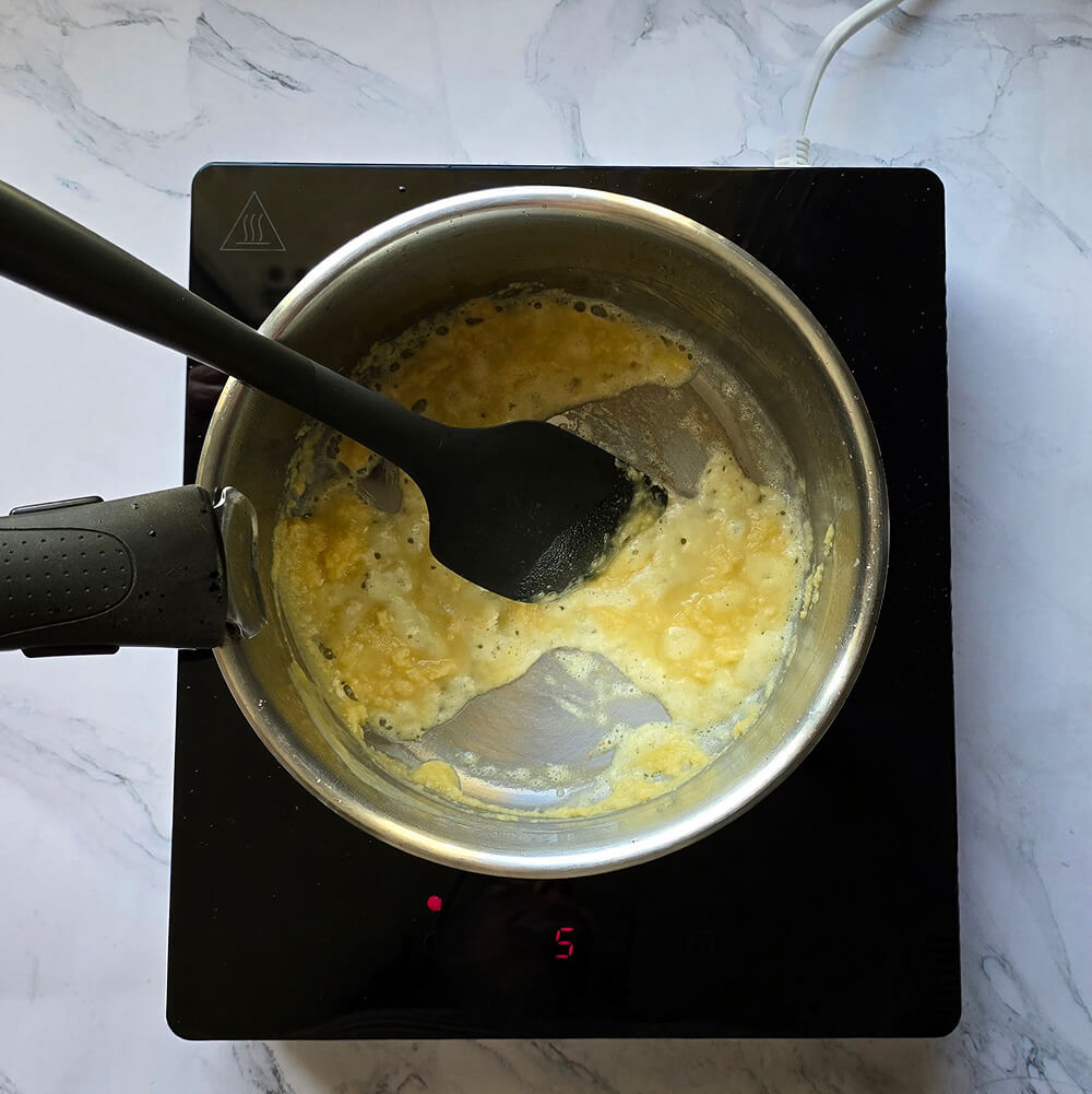 Mélange homogène de beurre fondu et de farine (roux) dans une casserole, remué avec une spatule noire sur une plaque de cuisson.