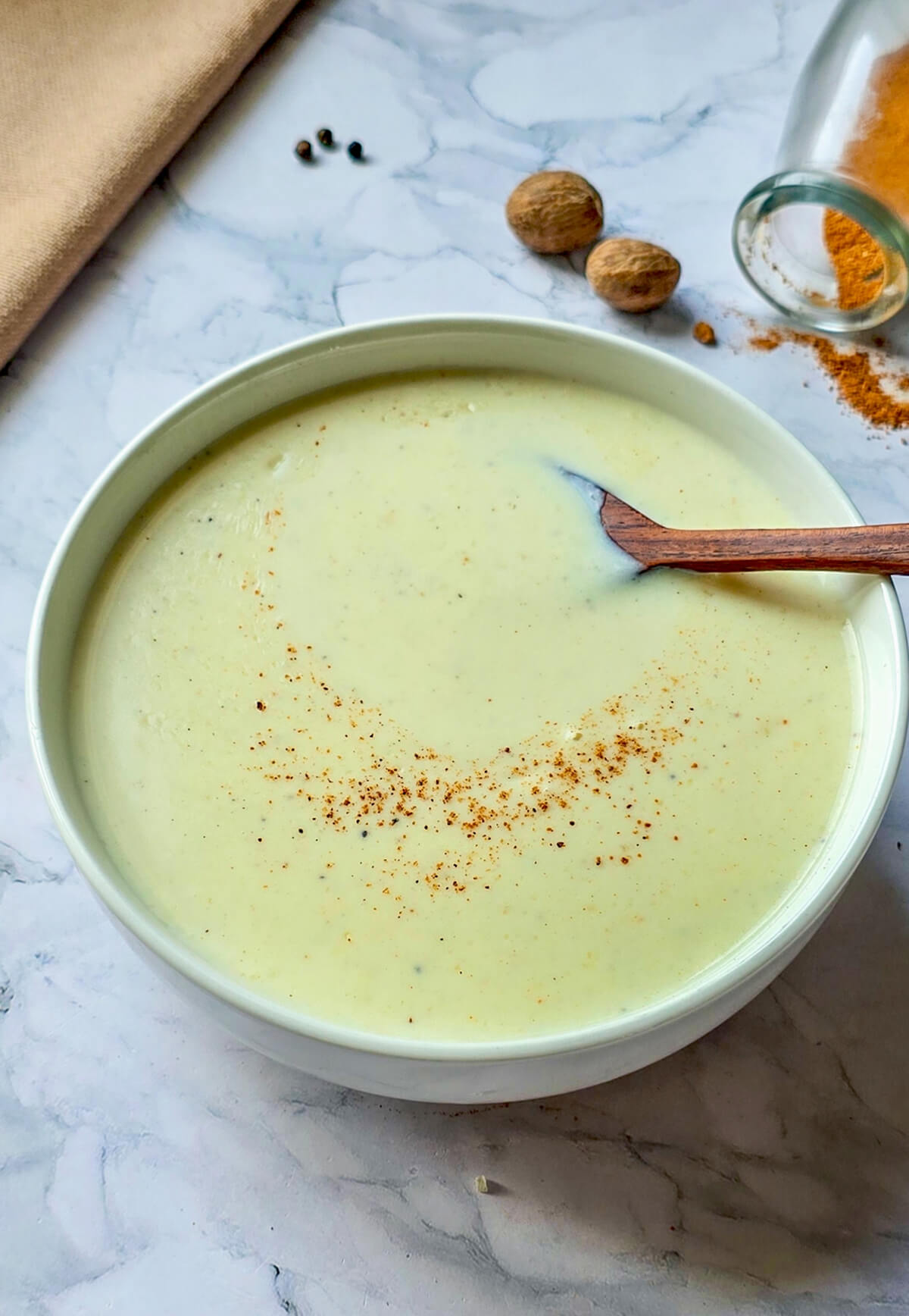 Un bol contenant de la sauce béchamel fait maison, sur fond marbré blanc, noix de muscade.