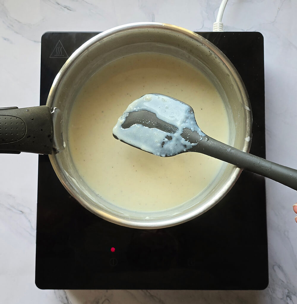 Sauce béchamel onctueuse et lisse dans une casserole, nappant une spatule grise pour montrer sa texture parfaite après cuisson.