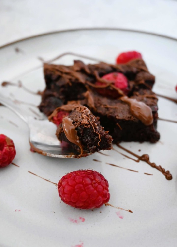 Un morceau de brownie sur une cuillère et une framboise.