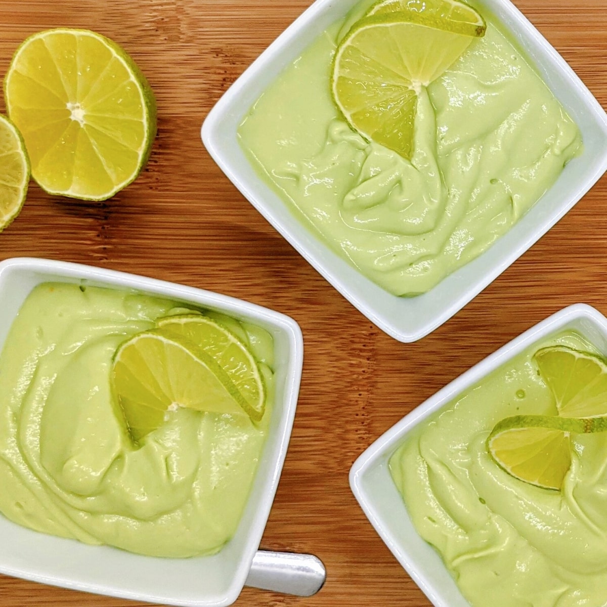 Des ramequins blancs remplis de crème avocat citron vert sur une planche en bois.