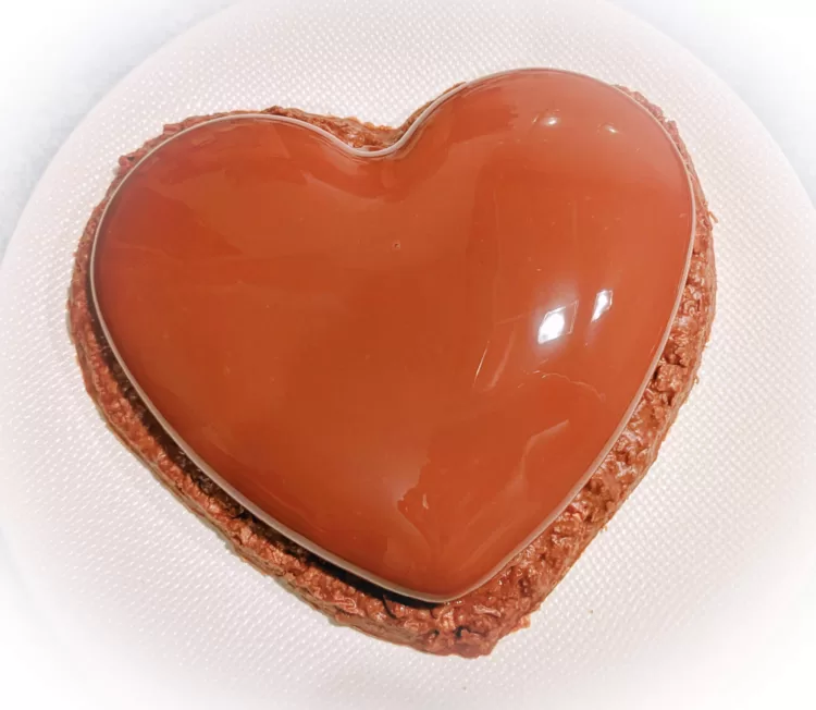 Un entremets au chocolat en forme de coeur dans une assiette blanche.