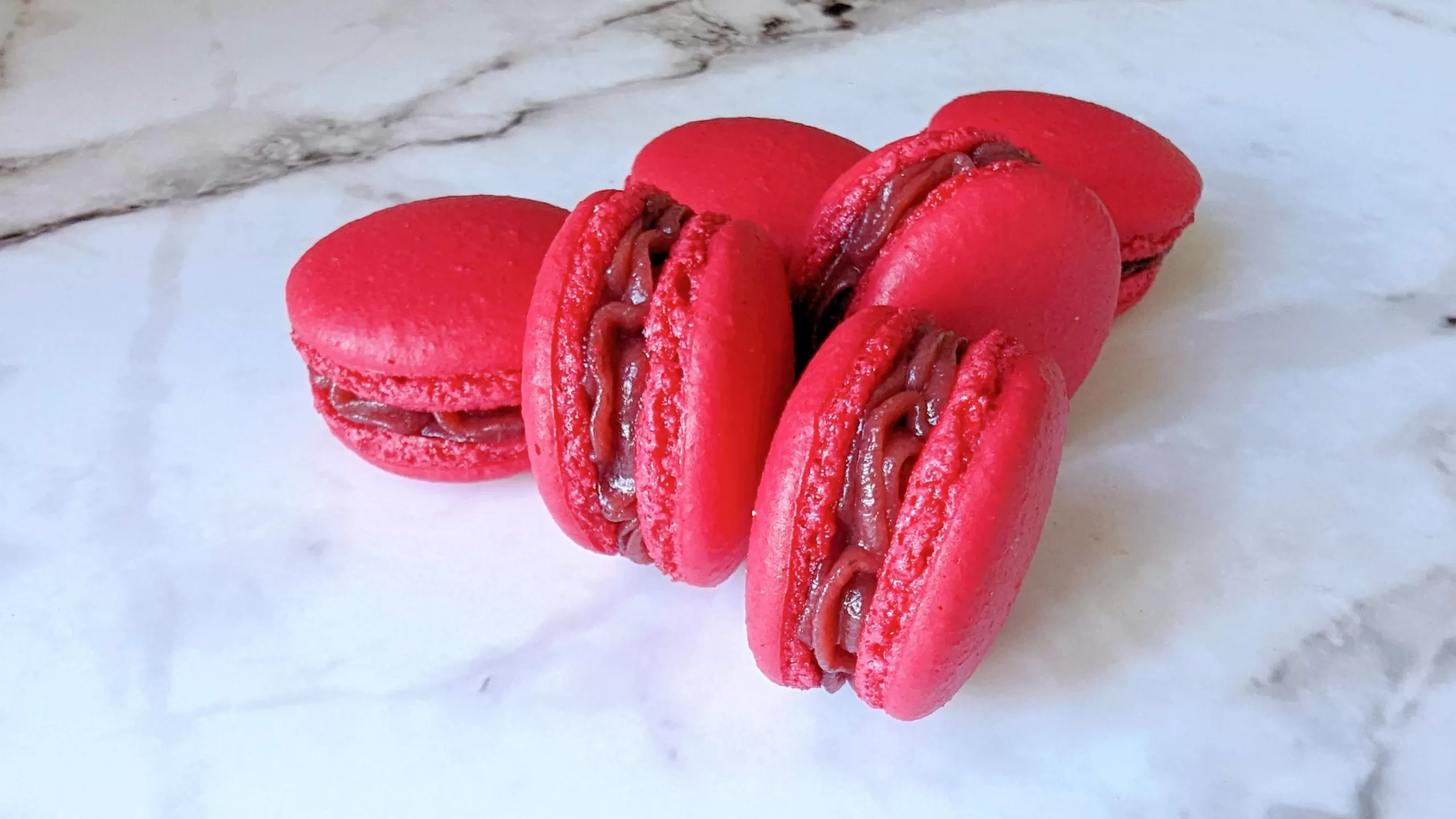 Des macarons à la framboise faits maison sur une surface blanche marbré.