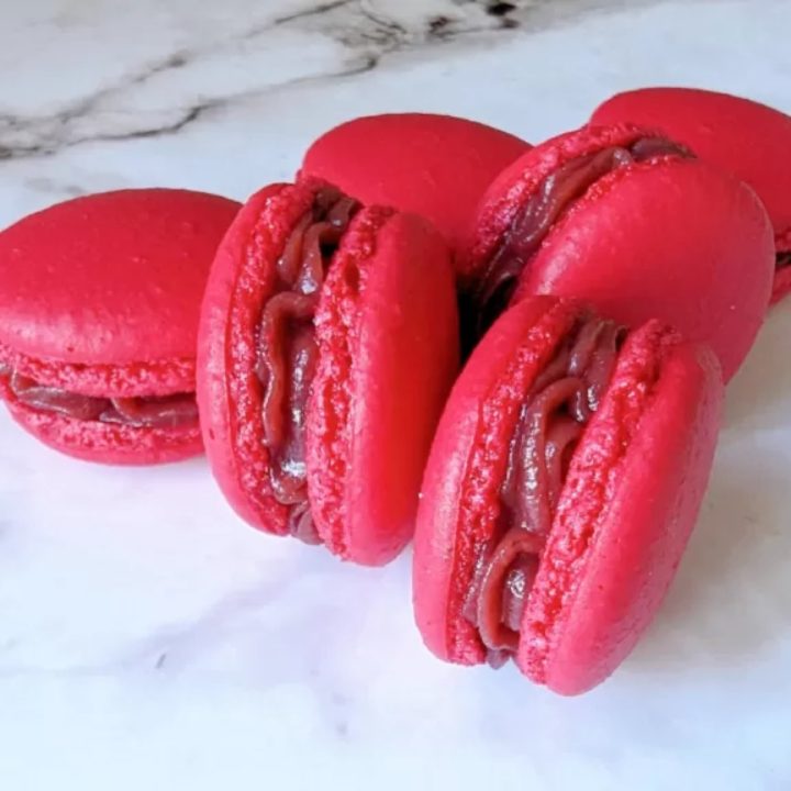 Des macarons tout framboise, sur un fond blanc marbré.