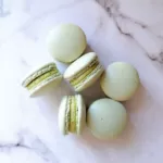 Des macarons pistache faits maison sur une surface blanche marbré.