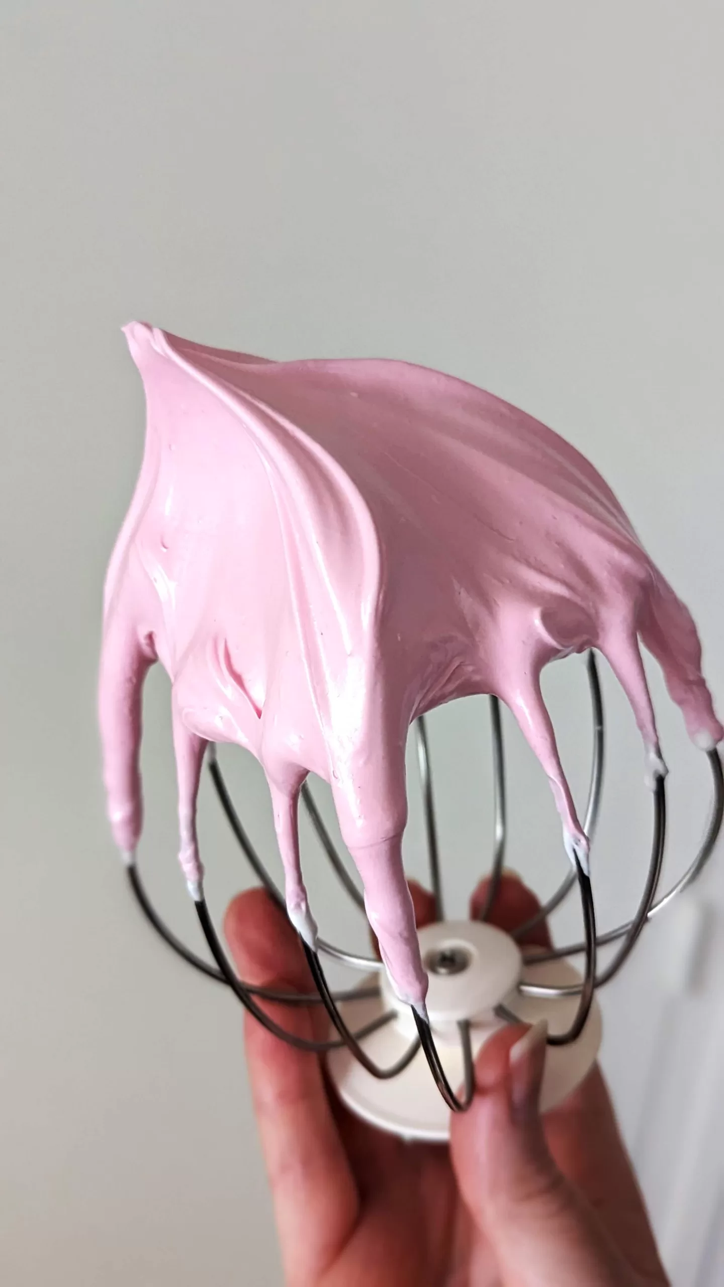 Une main tenant le fouet d'un robot culinaire, imprégné de meringue a l'italienne framboise.