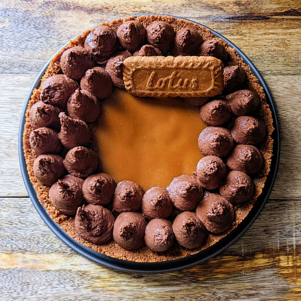 Une tarte chocolat spéculoos dans son moule rond, sur un fond en bois.
