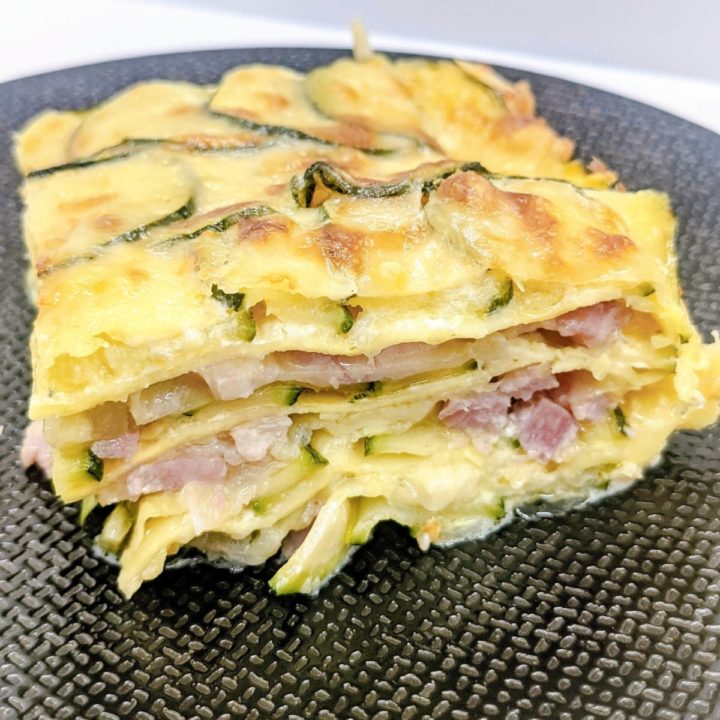 Une part de lasagne courgette jambon sur une assiette noire.