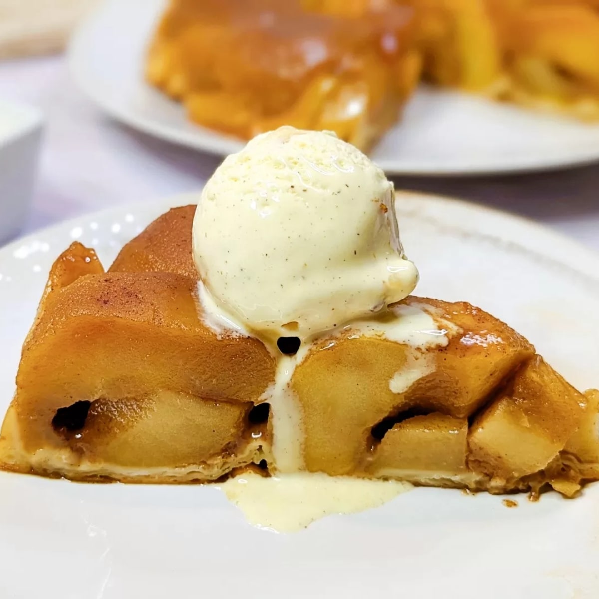 Une part de tarte tatin avec une boule de glace sur le dessus.