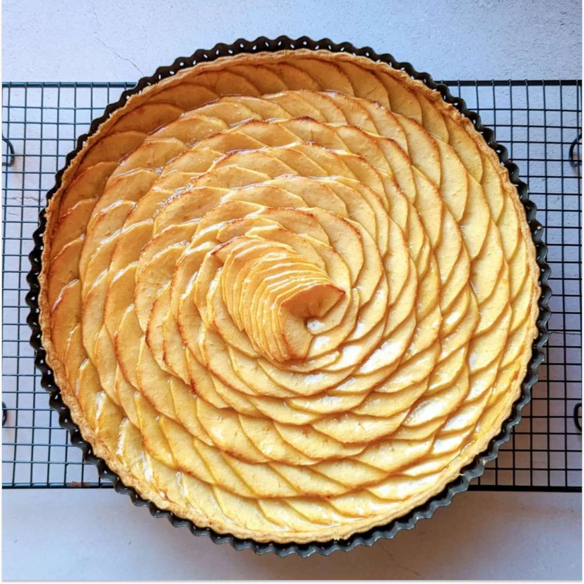 Une tarte aux pommes toute simple dans son moule, sur une plaque de refroidissement noire.