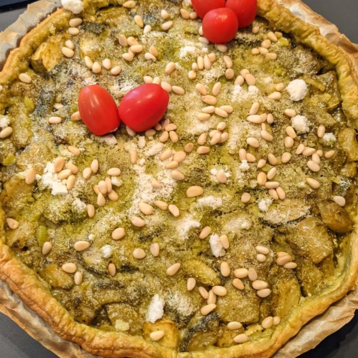 Une tarte pesto avec des pignons de pins et tomates cerises sur le dessus.