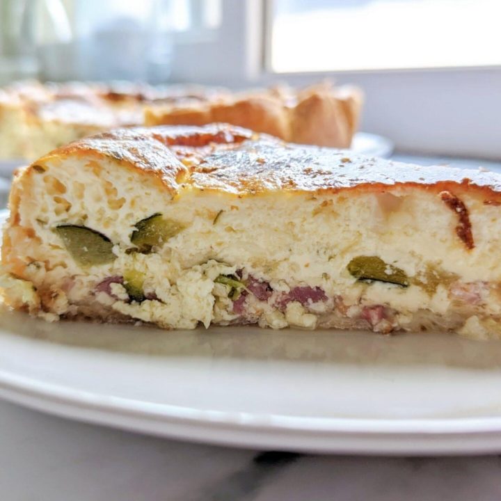 Une part de tarte salée courgettes et lardons dans une assiette blanche.