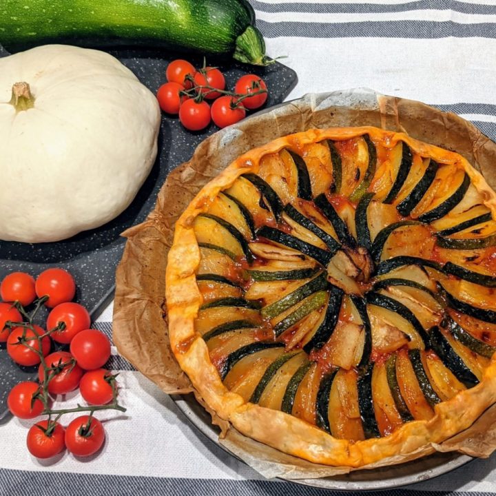 Une tarte salée patisson courgette avec patisson et tomates cerises sur le coté.