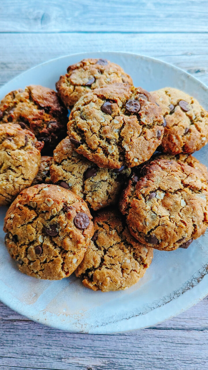 Des cookies beurre de cacahuète et pépites de chocolat dans une assiette blanche sur un fond de couleur bois.