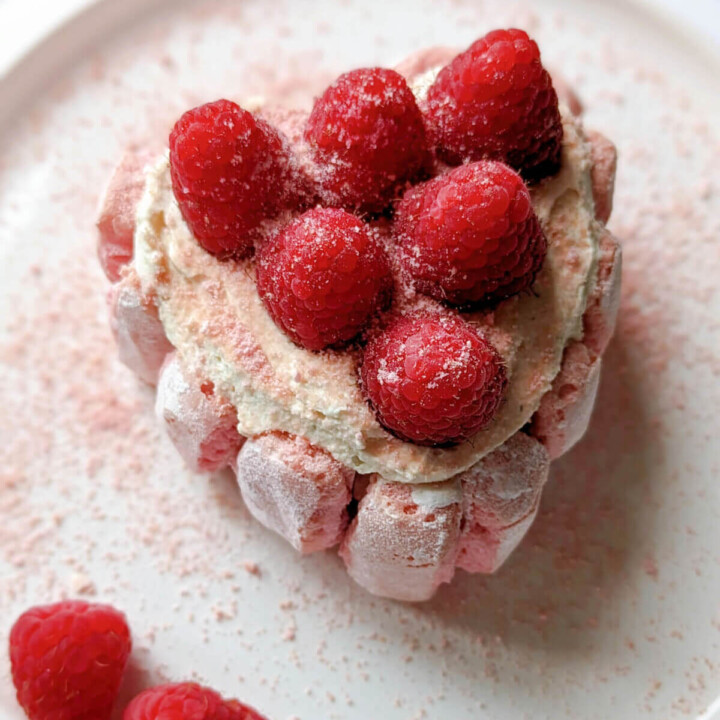 Une mini charlotte aux framboises en forme de coeur dans une assiette blanche, framboises sur le coté.