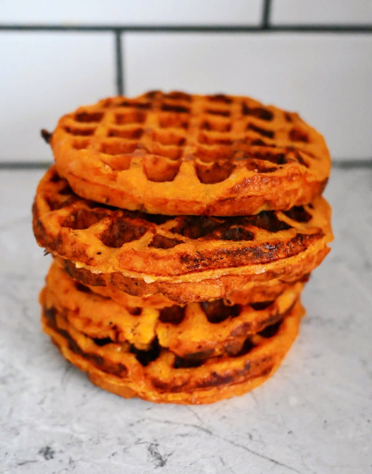 Des gaufres de patates douces empilées les unes sur les autres, sur un fond gris clair.
