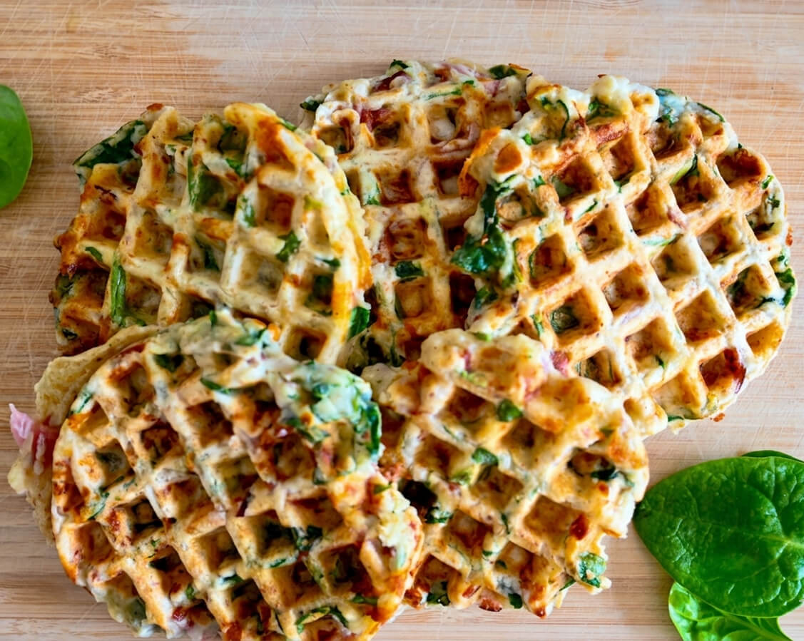 Des gaufres salées croustillantes au jambon-fromage sur une planche de bois avec quelques feuilles d'épinards.
