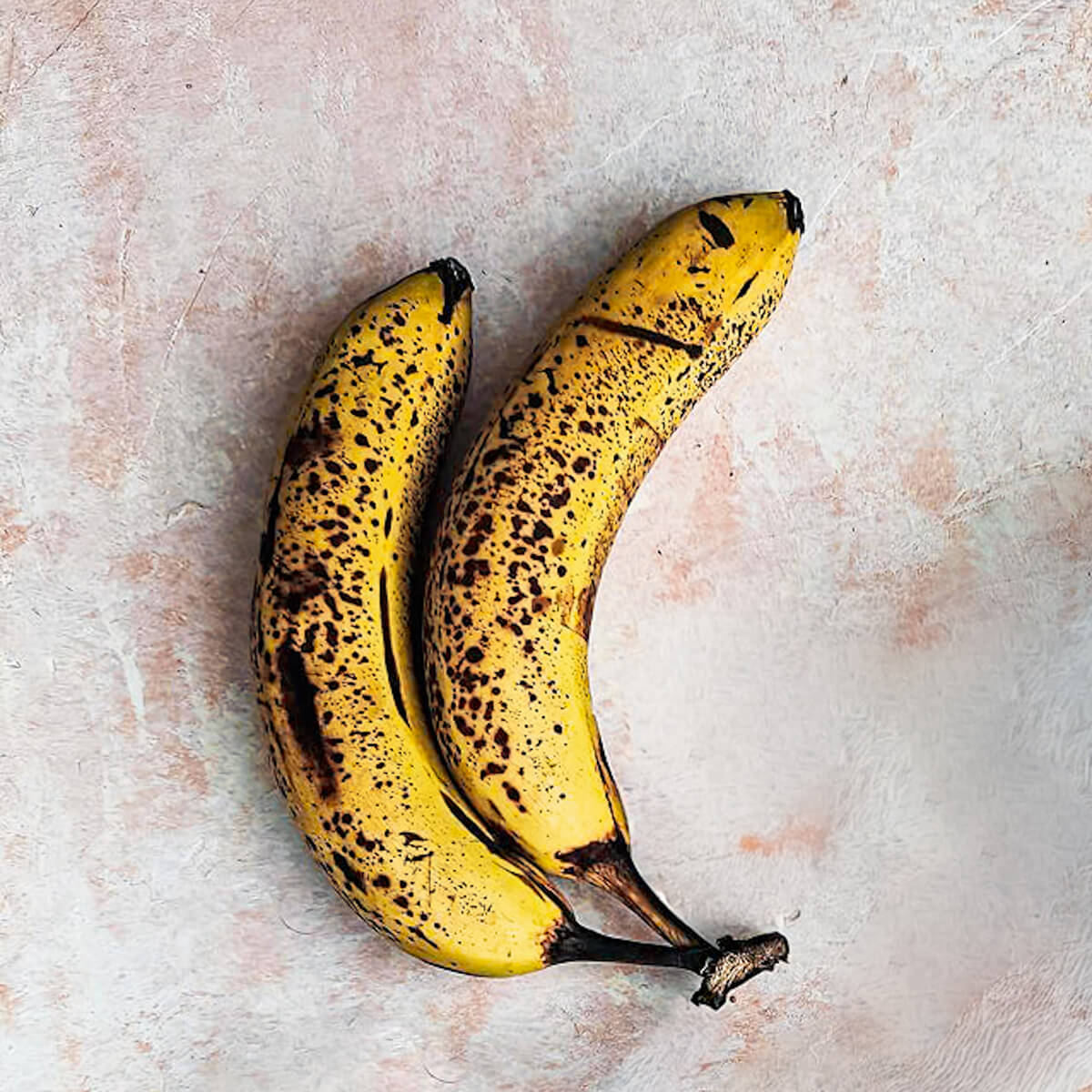 Deux bananes trop mûres sur un fond rose clair.