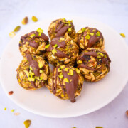 Des boules d'énergie chocolat pistache dans un bol blanc, pistaches concassées sur le coté.
