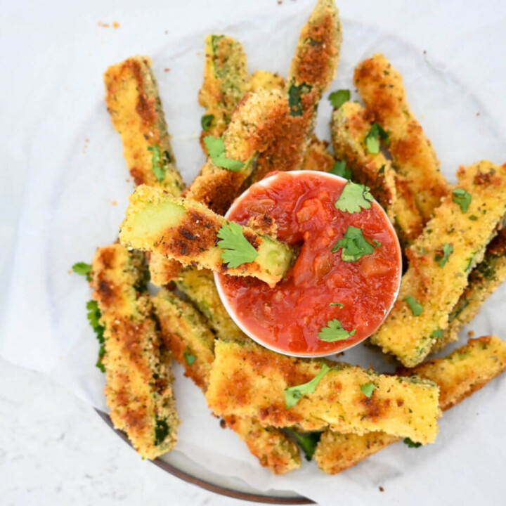Des frites de courgettes dans une assiette, sauce tomate au milieu.
