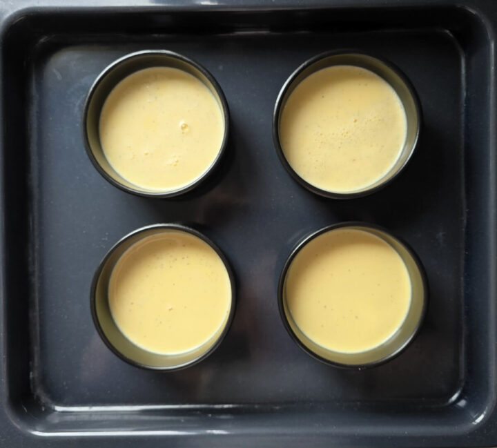 4 ramequins noirs remplis de crème brûlée, sur une plaque de cuisson noire.