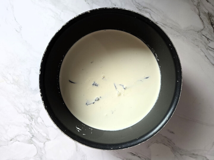 Mélange de crème liquide et gousse de vanille dans une casserole sur un fond marbré gris clair.