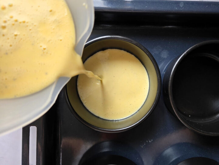 Une main versant de la crème liquide dans des ramequins noirs.