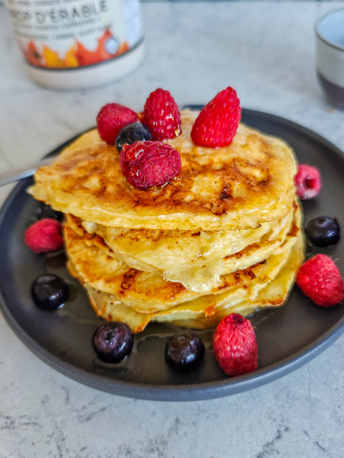 Des pancakes protéinés sur une assiette noire avec des fruits rouges autour.